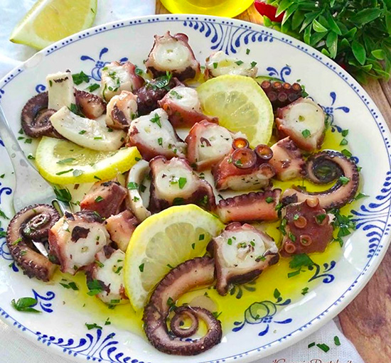 a plate of octopus with lemon slices and herbs